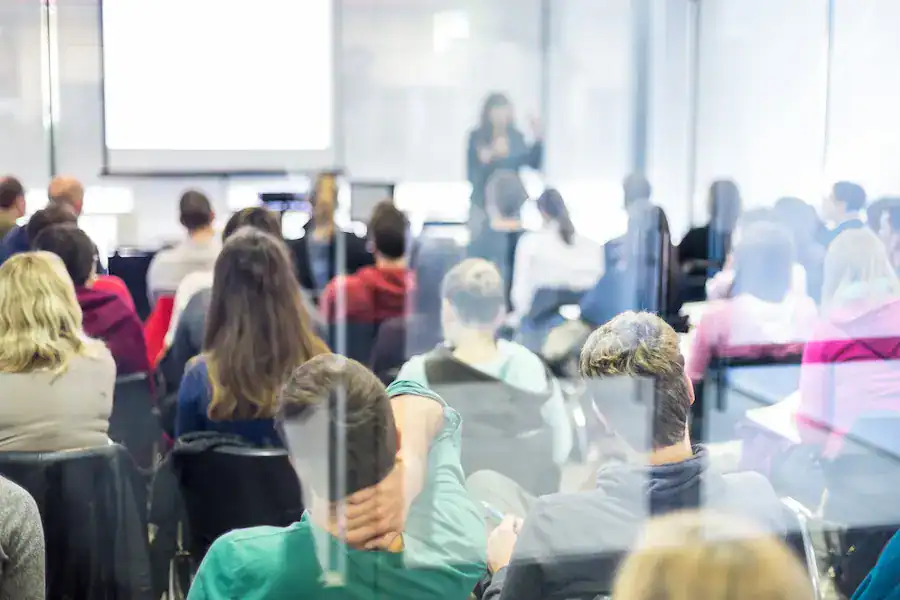 A group of individuals seated in a classroom, facing a speaker at the front near a projection screen.